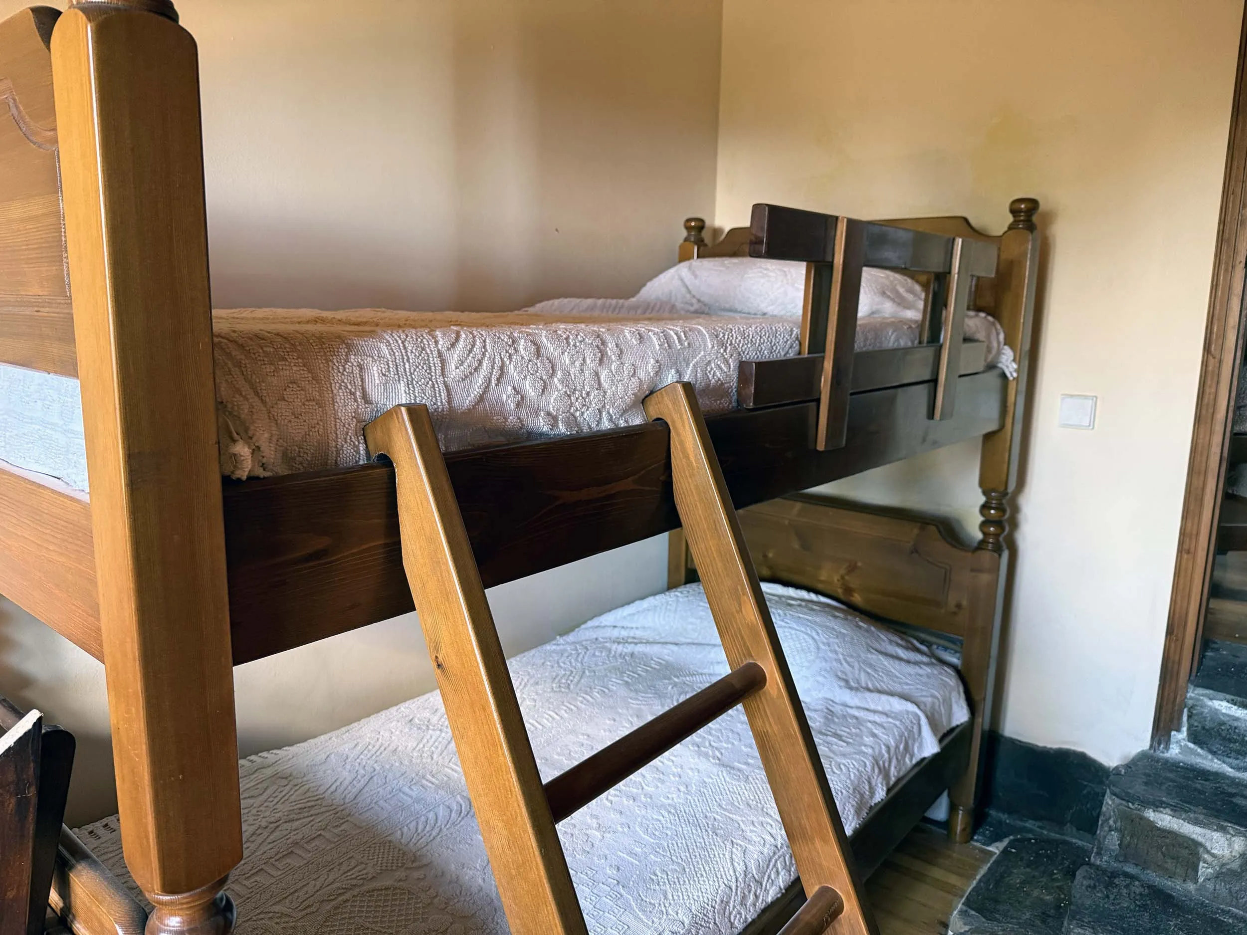 Wooden bunk beds in a twin room with natural light and stone tile flooring