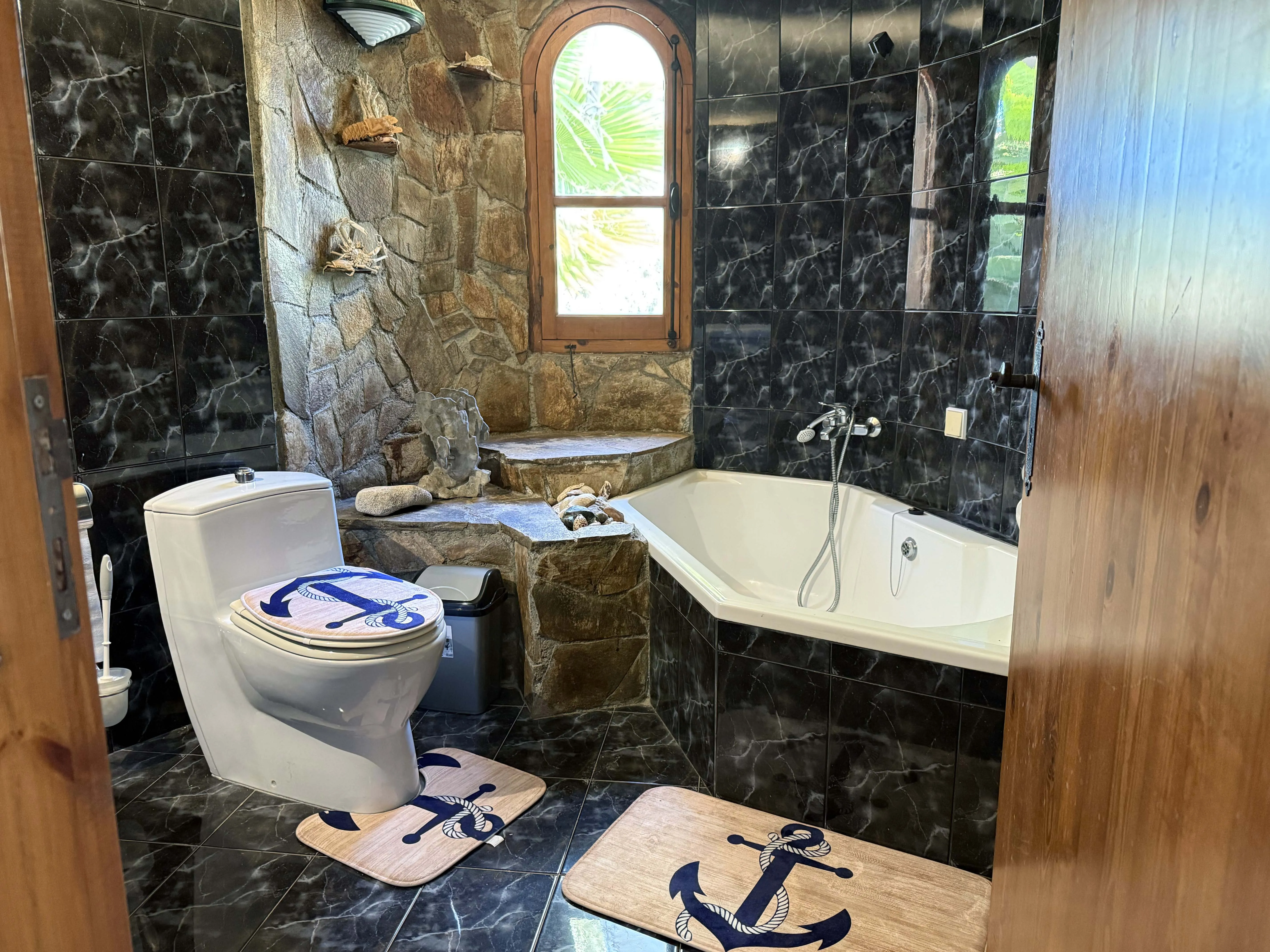 Nautical-themed bathroom with stone walls, corner bath and anchor motif accessories